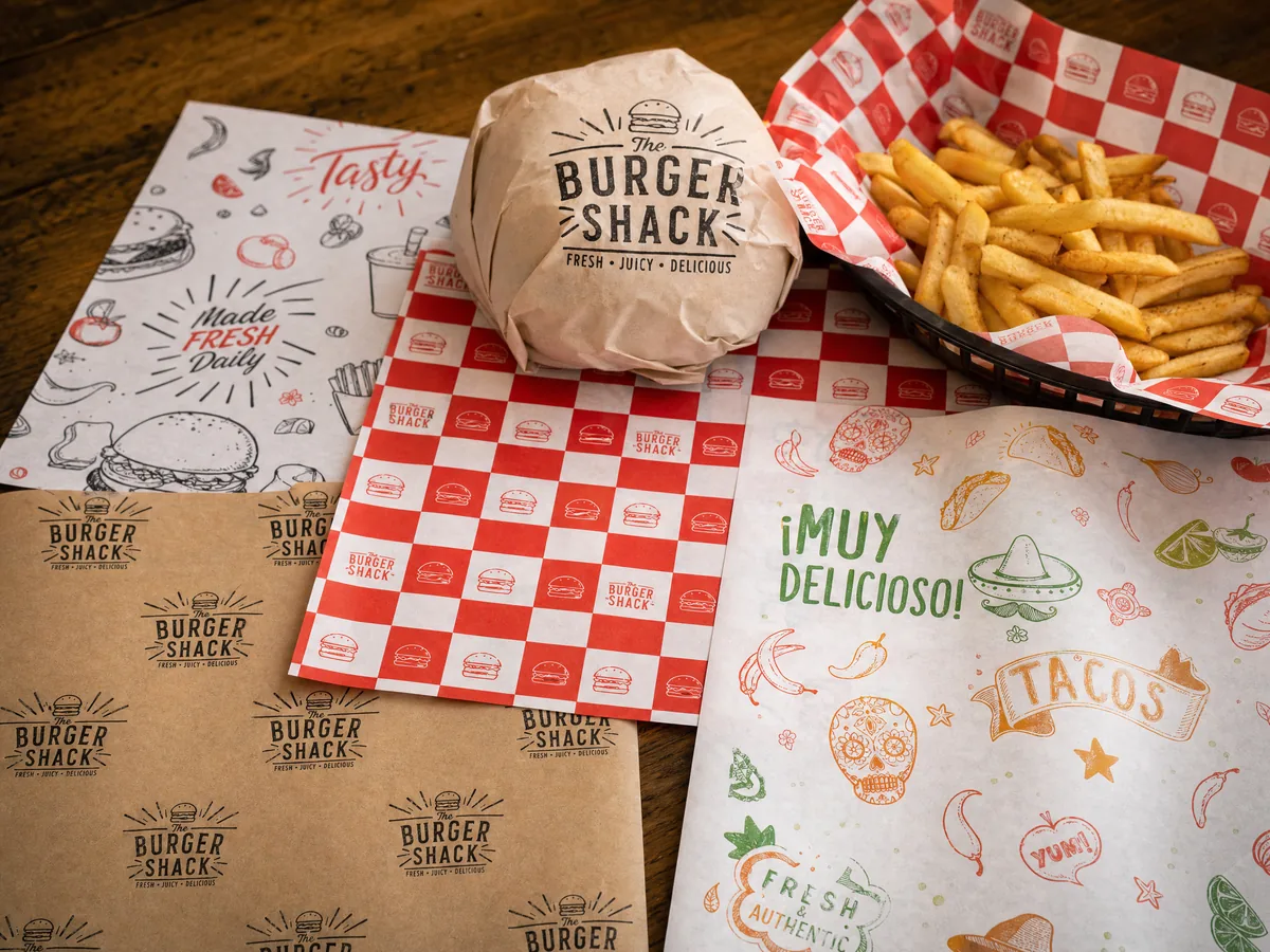 Custom printed deli paper sheets with brand logos and patterns — burger wrapper, checkered pattern, illustrated food graphics — CupsPak custom deli paper printing