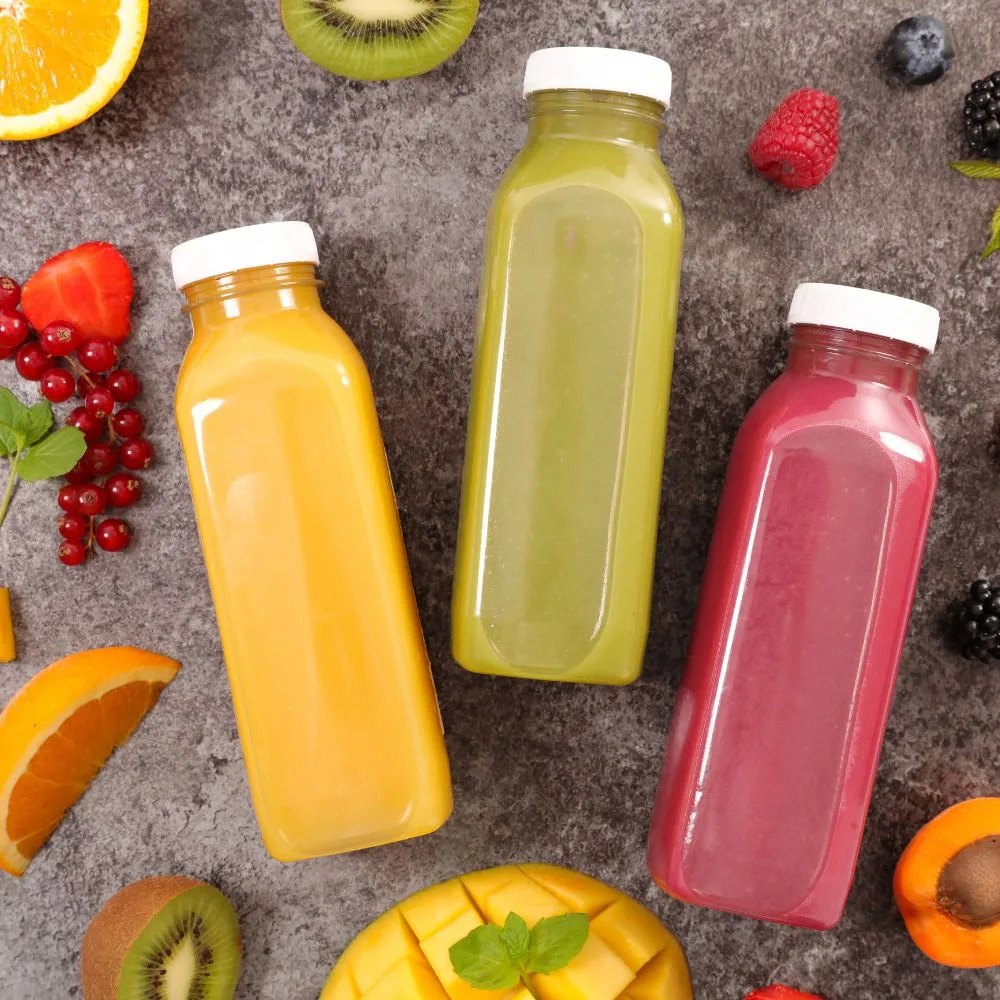 Square PET juice bottles with white caps in a flat-lay with fresh fruit, real production bottles, CupsPak