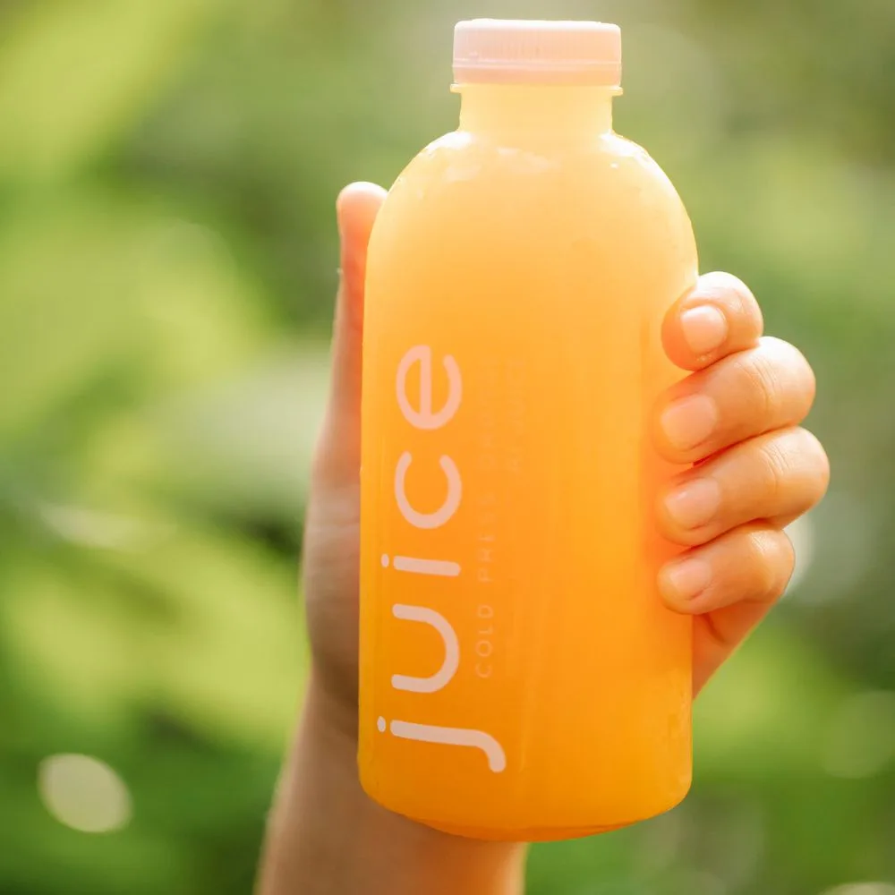 Hand holding a screen-printed PET juice bottle with white branding — direct bottle printing, no label peeling, CupsPak custom beverage bottles